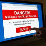 컴퓨터 화면에 악성 자바스크립트 코드 경고 메시지가 표시되어 있고, 큰 빨간색 '차단' 버튼이 클릭되는 모습이다.